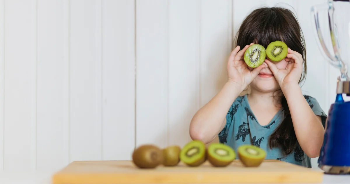 little girl holding cut kiwi's up to her face
